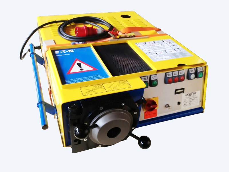 Walform machine seen from three quarters, with the blue carrying handles, the mains cable and red three-phase plug stowed on the lid, and the operating placard